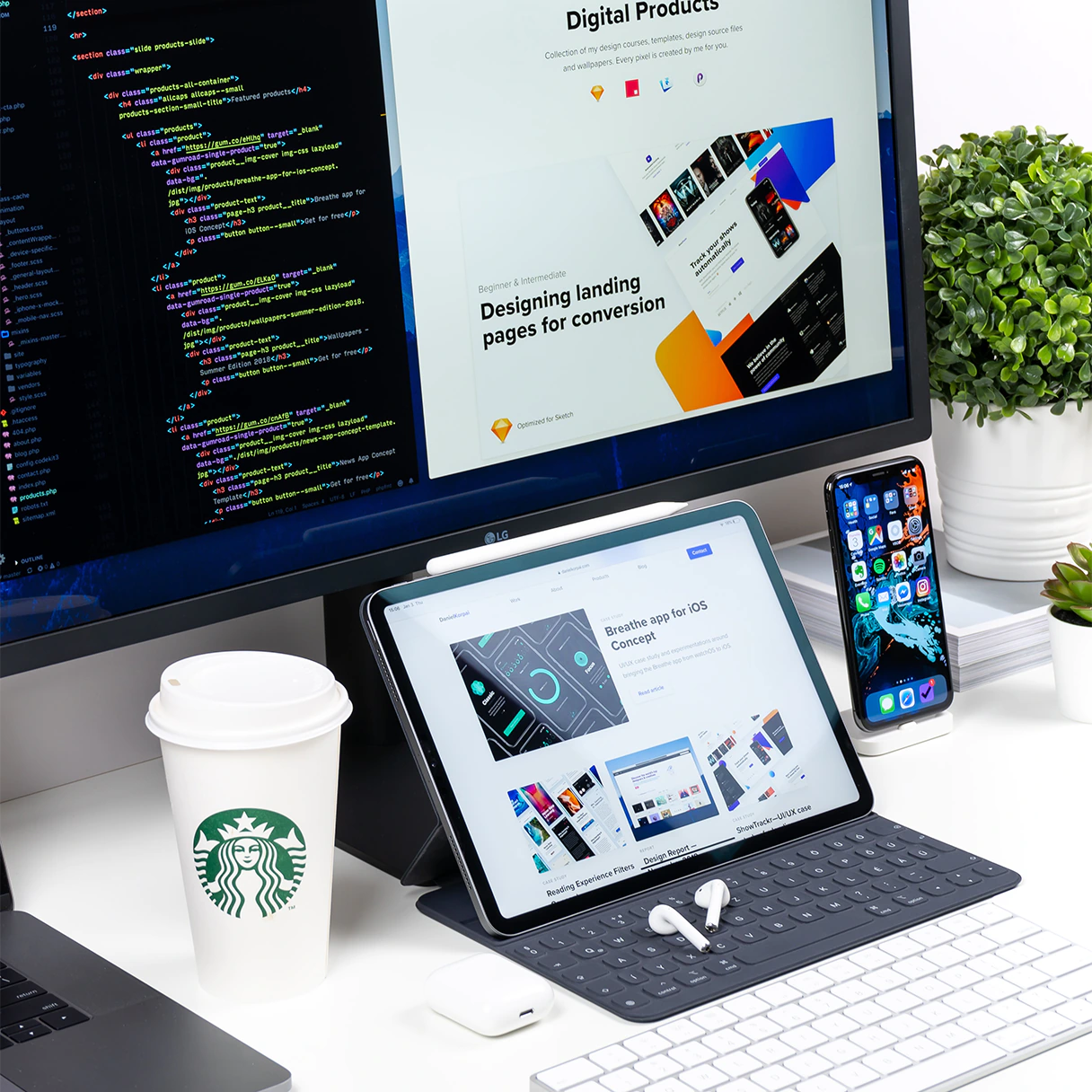 Schreibtisch eines Webentwicklers auf dem ein LG Bildschirm, iPad Tablet mit Tastatur, iPhone Smartphone und Starbucks Cafe steht.